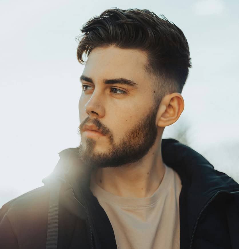 Moderner Mann mit gepflegtem Haarschnitt und Bart, Blick in die Ferne.