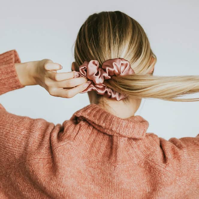 Frau bindet ihr langes Haar mit einem rosa Haargummi.