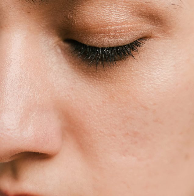 Nahaufnahme eines Gesichts mit reiner Haut und glatter Textur, Fokus auf Wange und Augenlid.