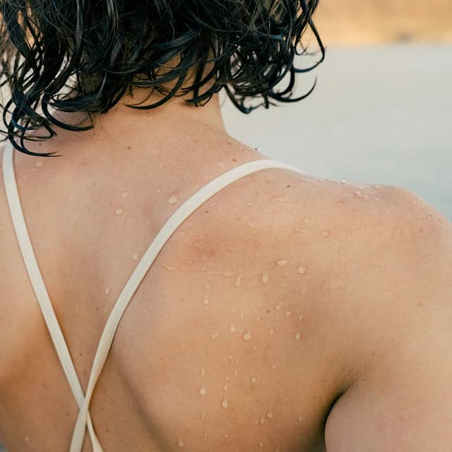 Frau mit nasser Haut nach Sauna oder Schwimmen, Hautpflege im Fokus.